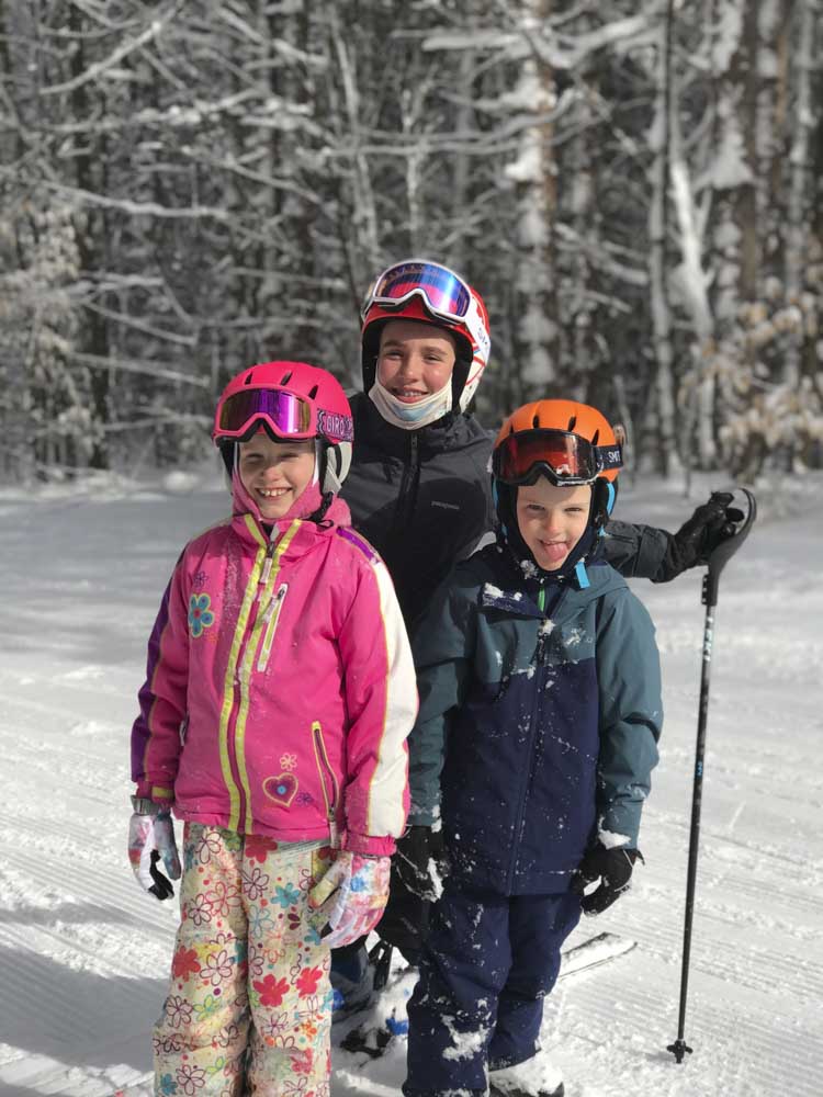 three children wearing skis standing in the snow