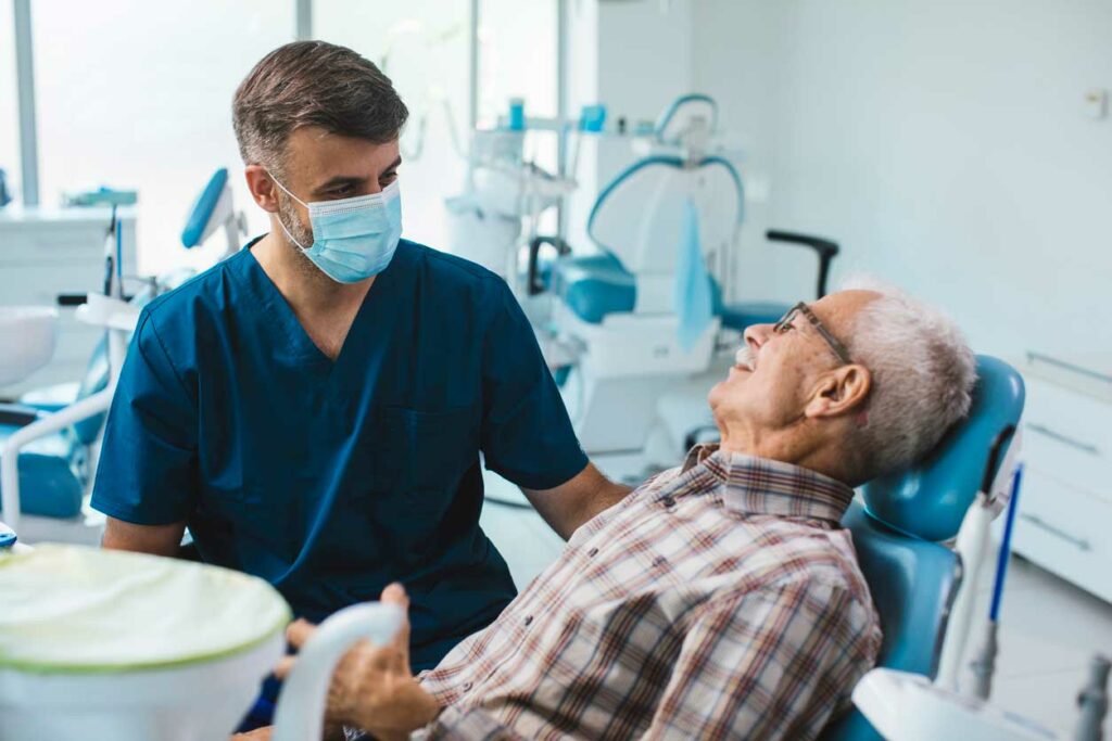 dentist speaking with older male patient as he sits in the dental chair