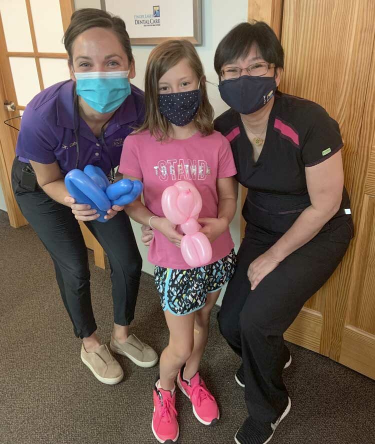 Team members of Finger Lakes Dental with a pediatric patient holding balloon animals