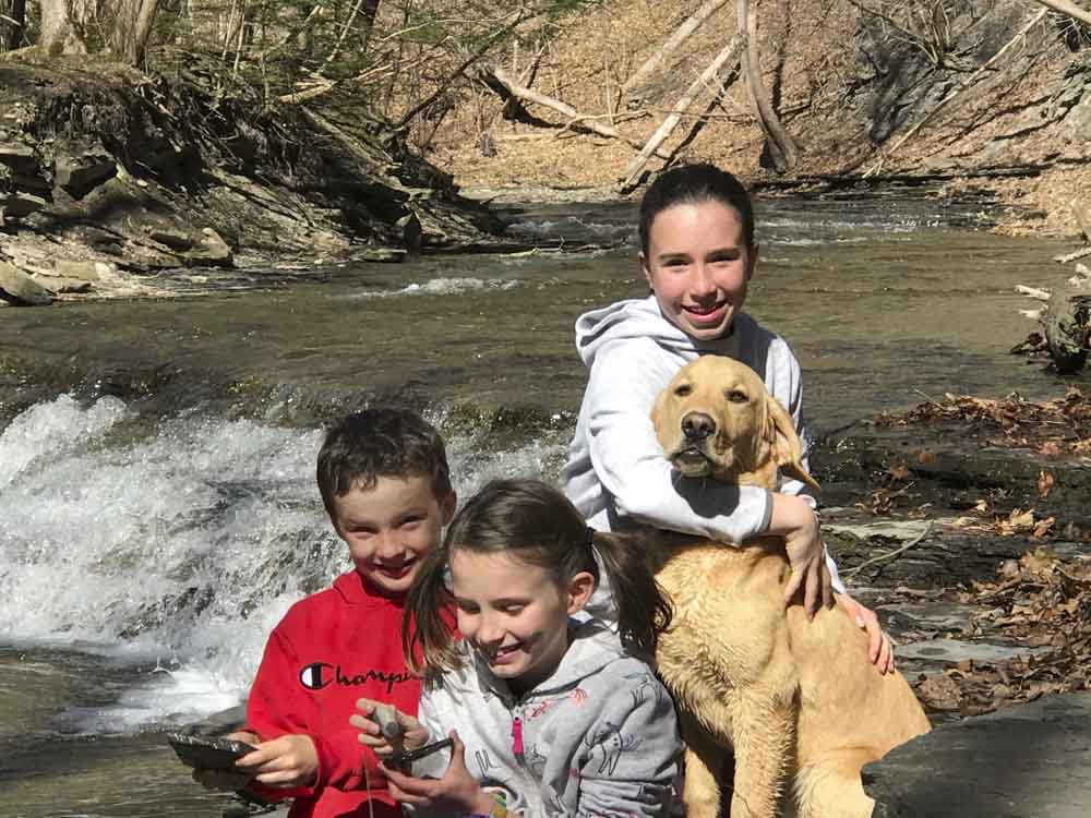 three children and a dog sitting by a river