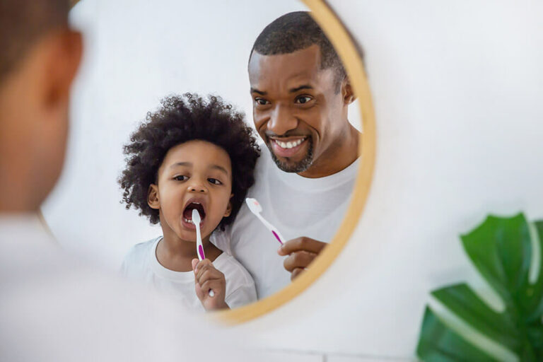 a dad teaching his son how to brush his teeth