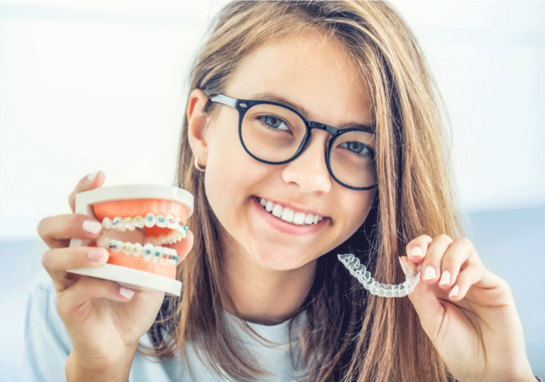 Young girl holding clear aligners in her right hand and metal braces in her left hand.